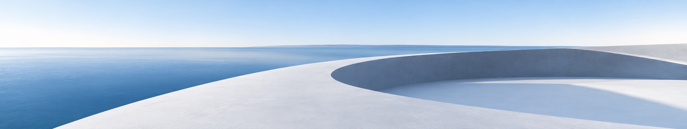 A curved pale stone terrace beside calm blue water.